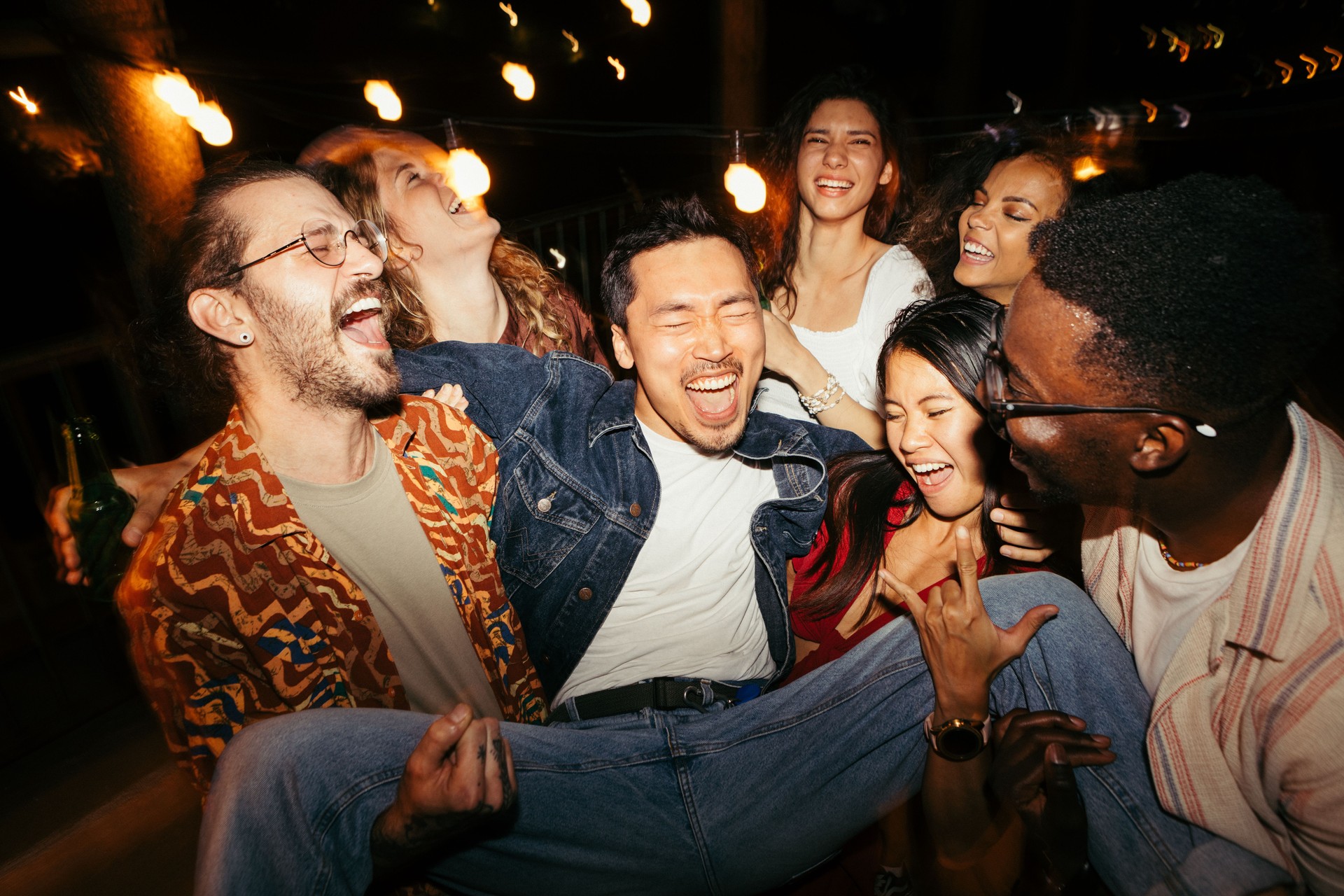 Los amigos levantan a su amigo masculino en la fiesta nocturna al aire libre en la azotea.